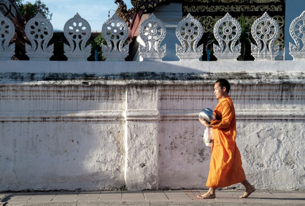 Thai Monk in orange clothes walks by a white wall in chiang mai, thailand