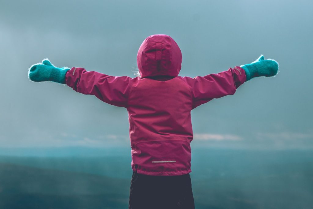 A hiking kid spreading its arms and watching a beautiful view.