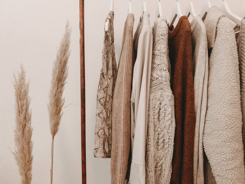 Clothes in beige tones hanging in an open closet.