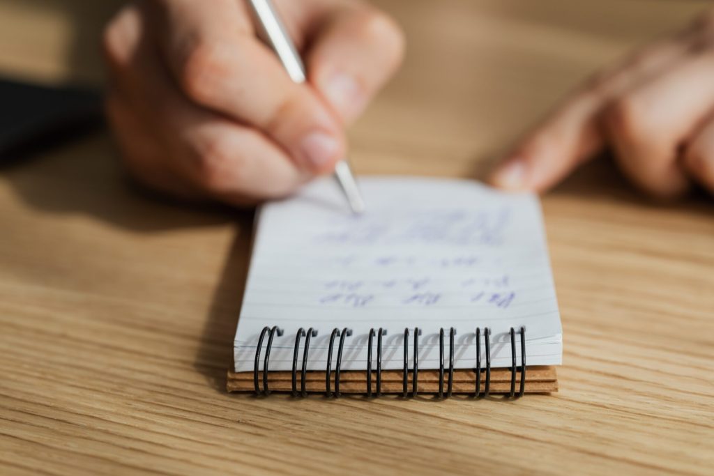 A man writing something into a small white notebook with a black pen.