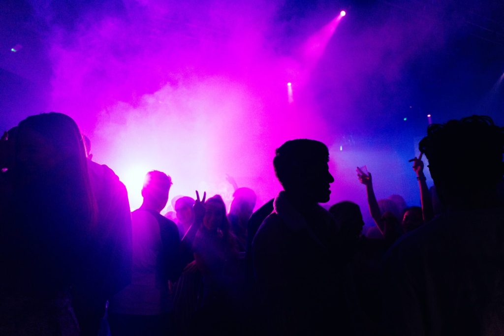 A party crowd dancing in a club with purple smoke.