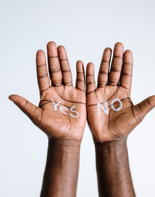 Two hands in front of a white wall, written yes and no on each hand.