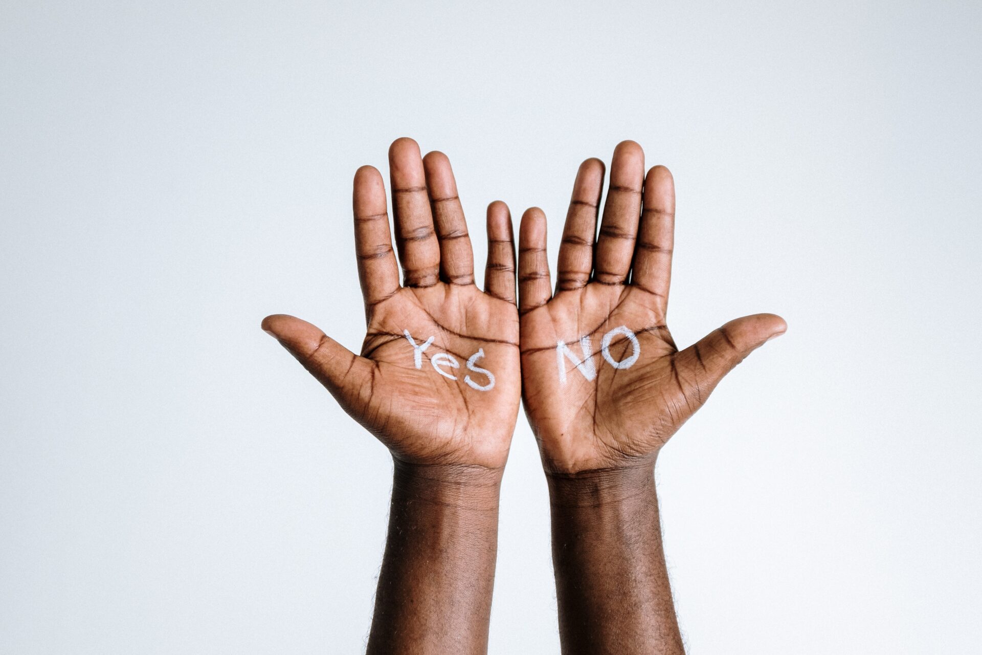 Two hands in front of a white wall, written yes and no on each hand.