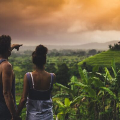 young couple from behind standing in front of a green valley in Bali, he is pointing to something far away