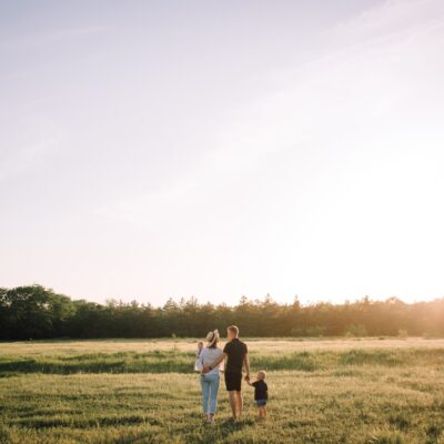 Family of three from behind, walking on a field of gras.