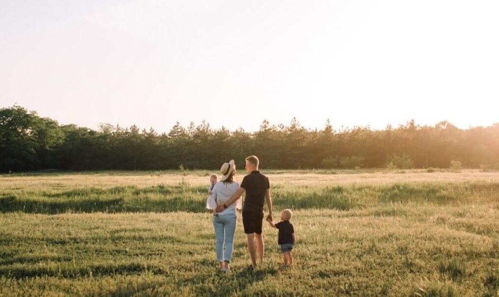 Family of four from behind, walking on a field of grass.