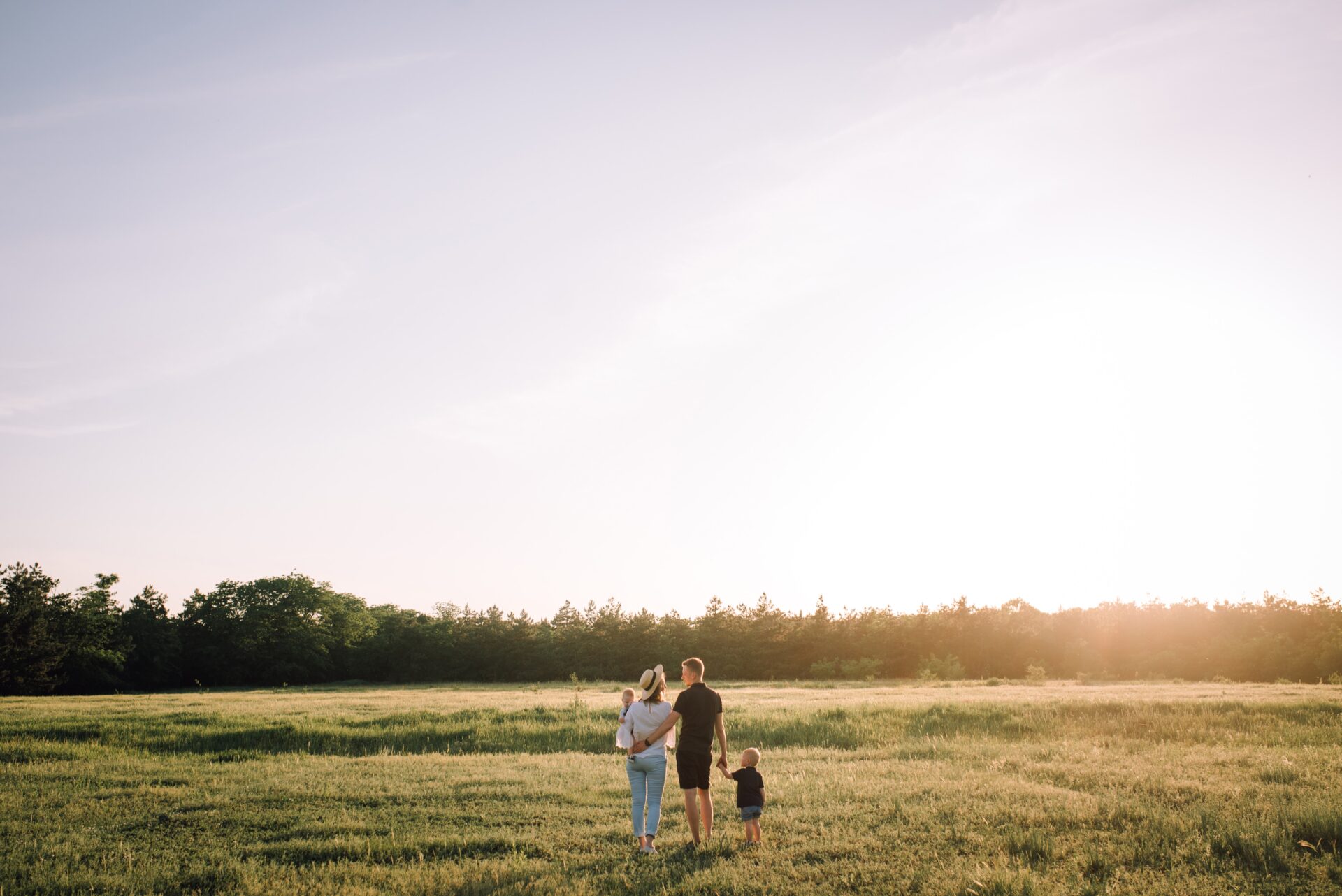 Family of three from behind, walking on a field of gras.