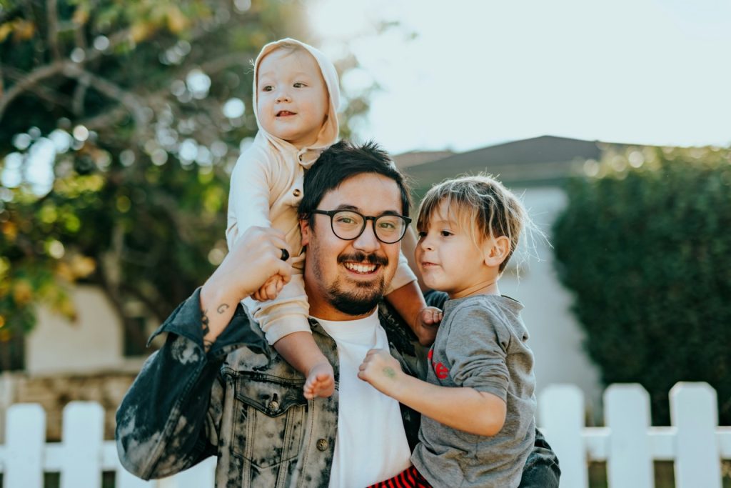 Father carrying two small kids and smiling into the camera