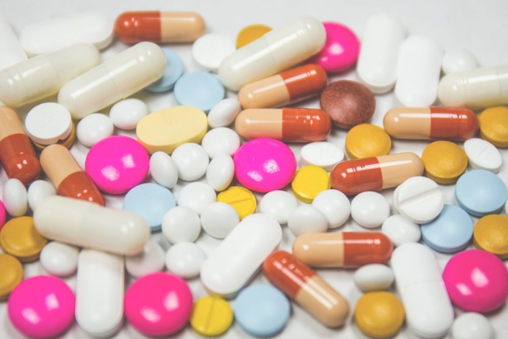 Pills in all different colors laying on a white table.