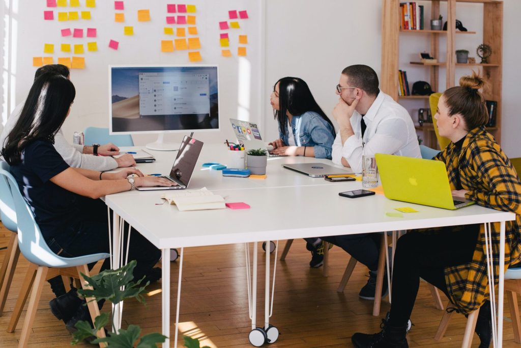 A group of colleagues sitting on a white desk, all staring at the display of a computer.