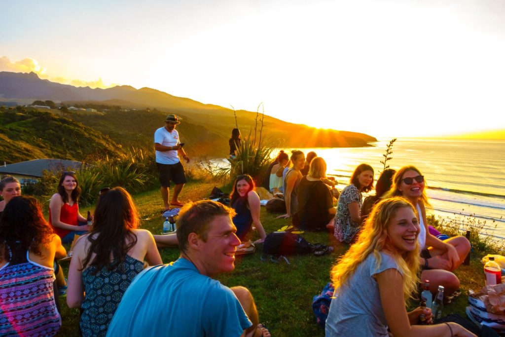 Crowd of Digital Nomad people sitting at the edge of a cliff at sunset.