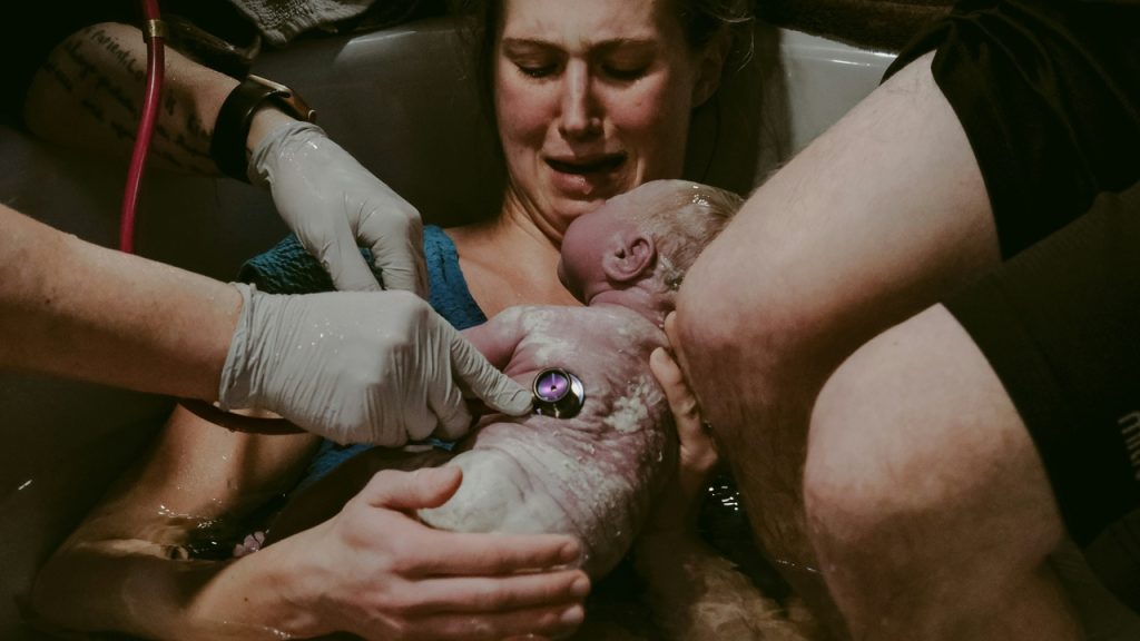 Homebirth in Thailand, Woman sits in birth bath tube and holds her freshly newborn on her chest