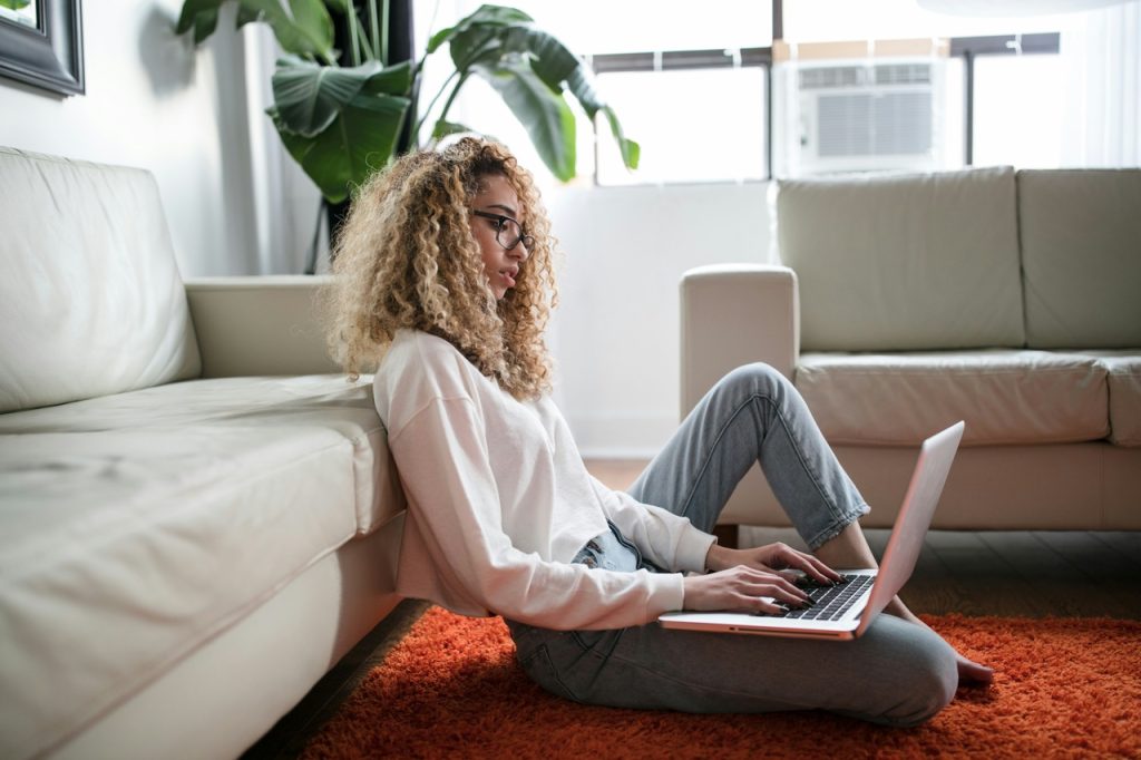 Woman working on laptop, sitting on the floor in front of the couch