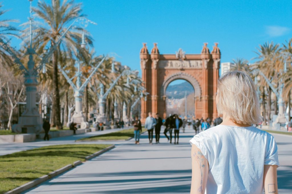 Person standing in front of an attraction, a big arch building