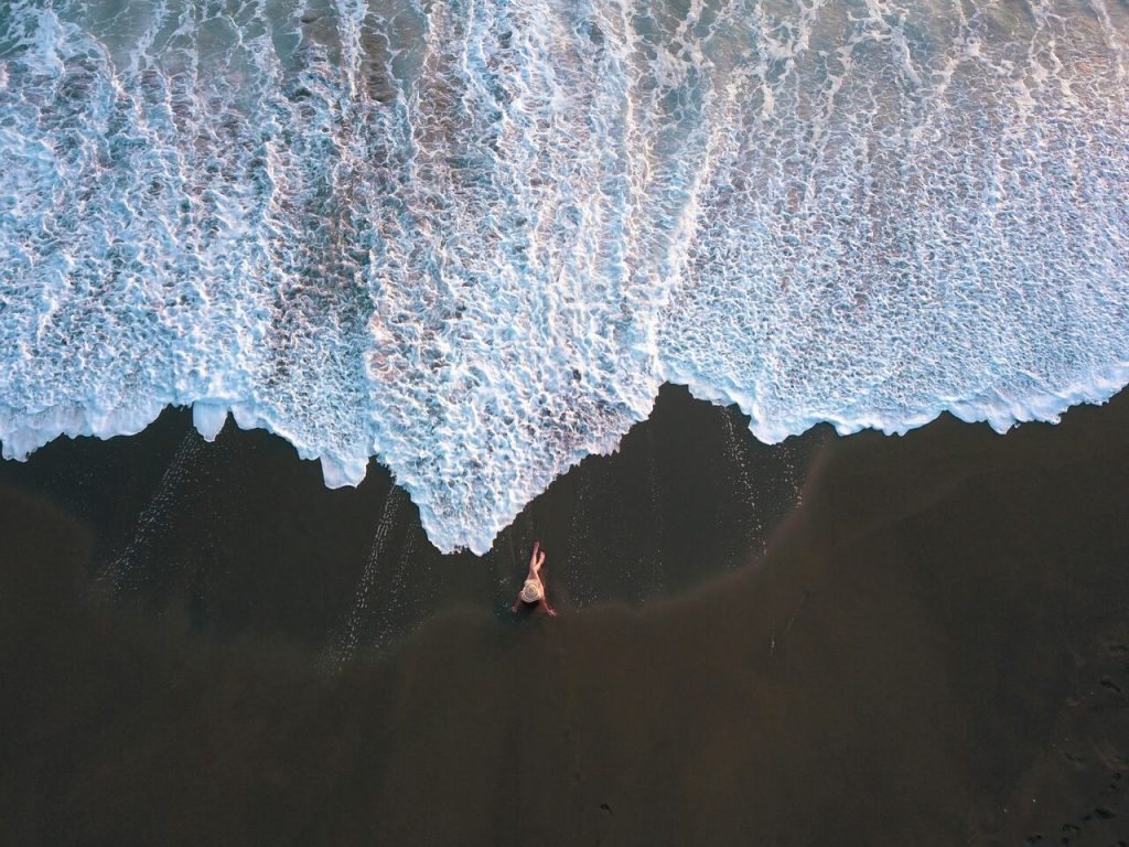 person sitting on a black sand beach in costa rica, view from above