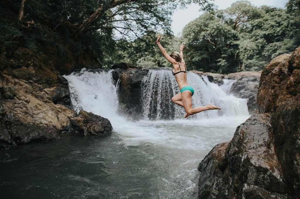 Woman in a green bikini jumping into a waterfall