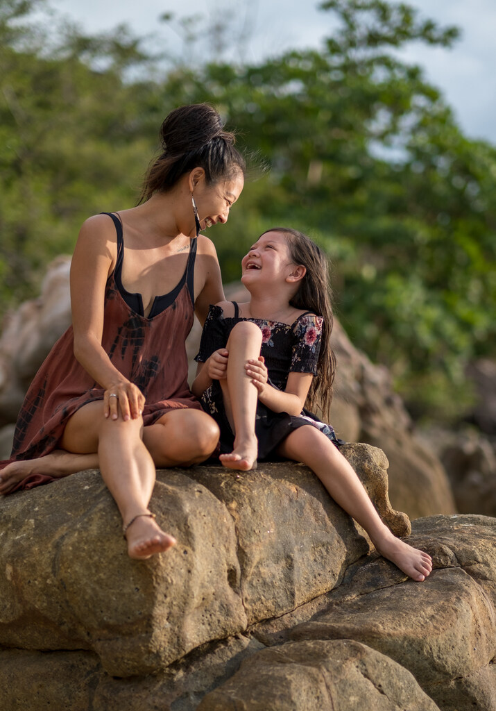 Mother and 8-yo daughter sitting on a rock and laughing at each other, digital nomad single mom, traveling as a single parent