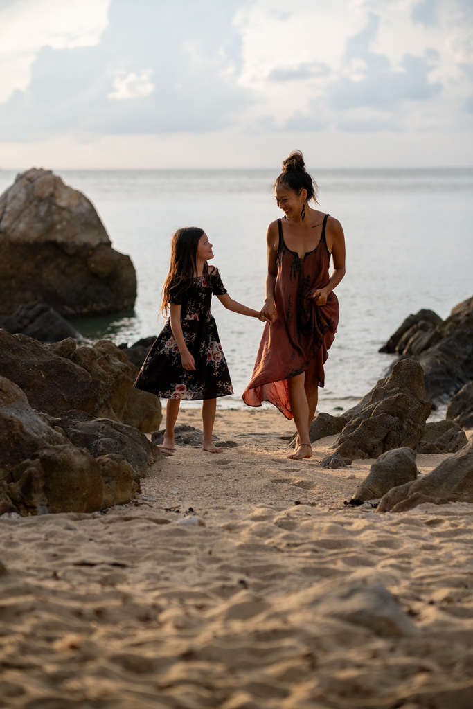 mother and daughter walking on a beach, holding hands, wearing summer dresses