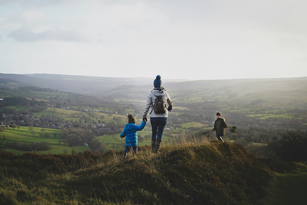 A mother hiking in a green landscape together with two small children