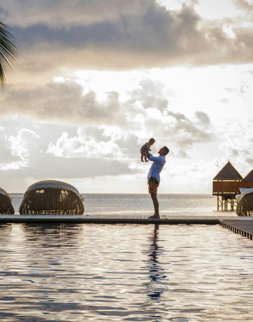 dad holds his toddler in the arms, standing at a pool, full time traveling families