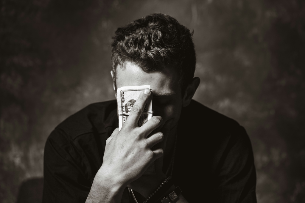 black and white portrait of young man holding usd bills in front if his face