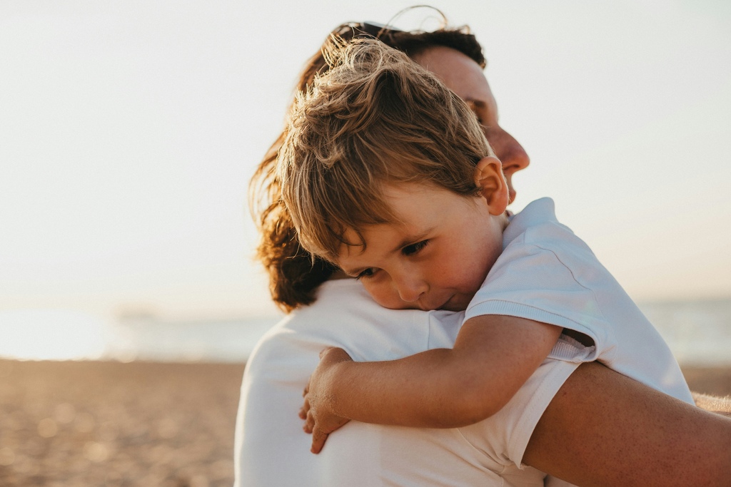 a mum hugging her toddler boy on the beach