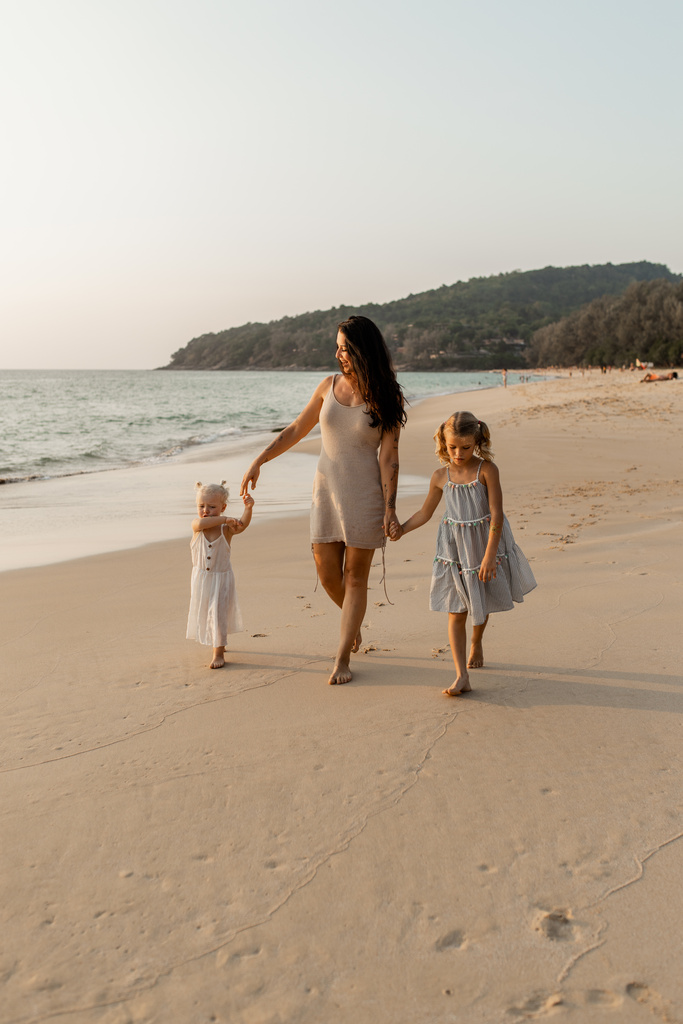 Mother with two little daughters walking on the beach.