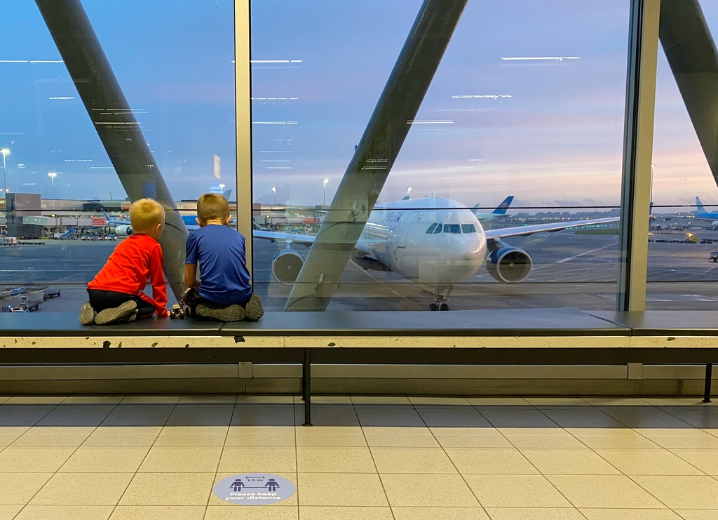 Two boys sitting at an airport window, watching an airplane, worldschooling tweens