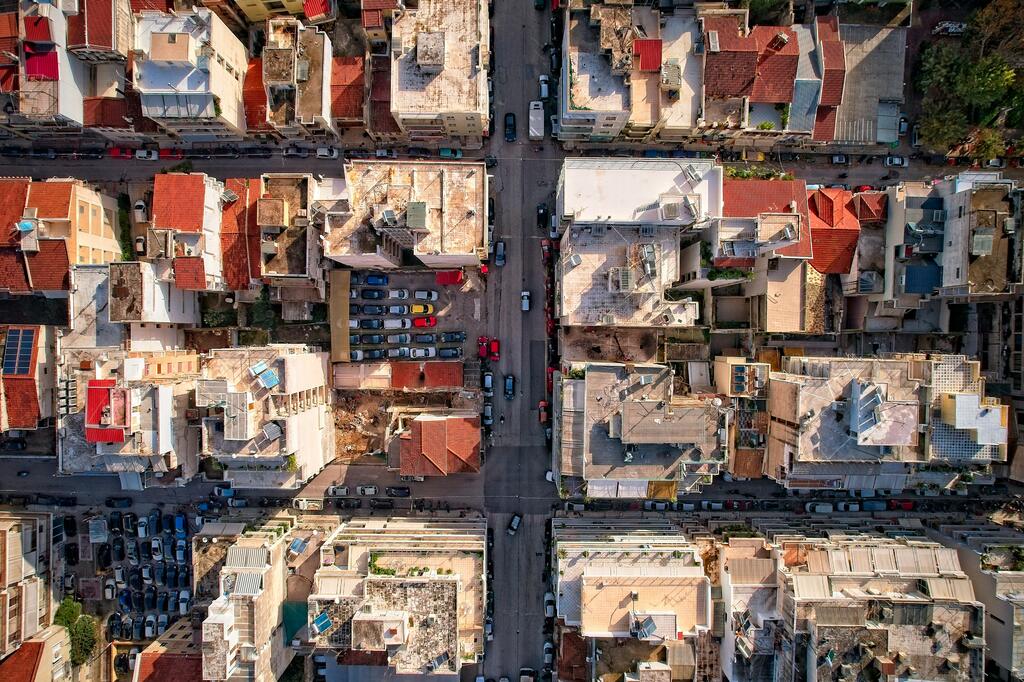 Aerial view of Patras, Greece, featuring a grid of residential buildings with red-tiled roofs and narrow streets filled with parked cars.