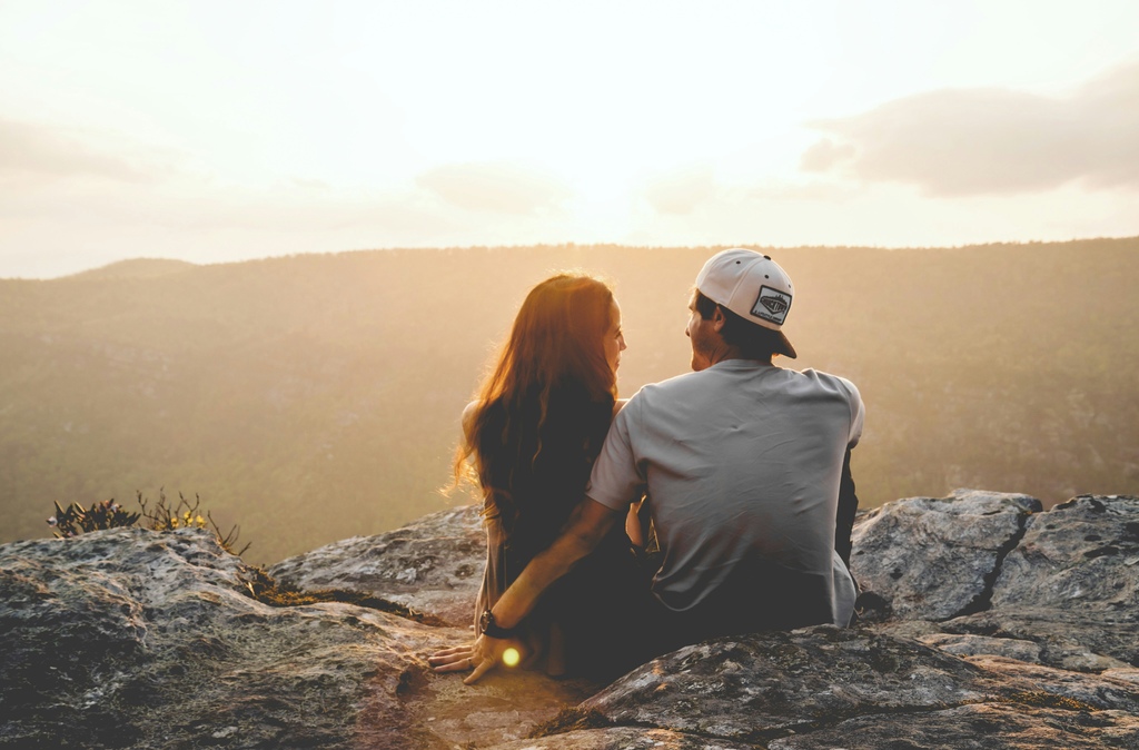 couple sitting on a hill and watching the sunset