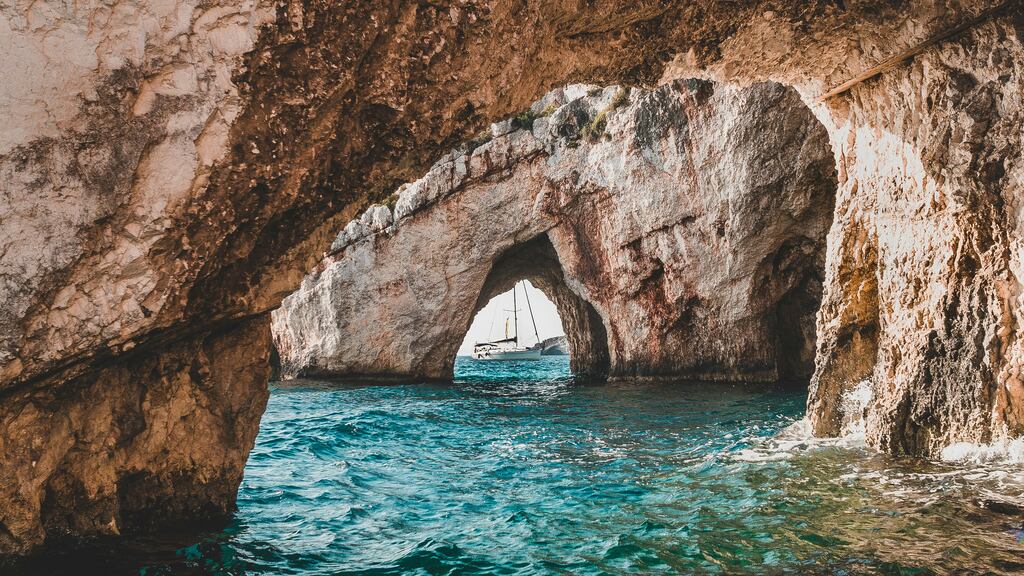 A view of the Blue Caves in Zakynthos, Greece, with clear blue waters flowing through natural rock arches and formations, creating a mesmerizing coastal landscape.