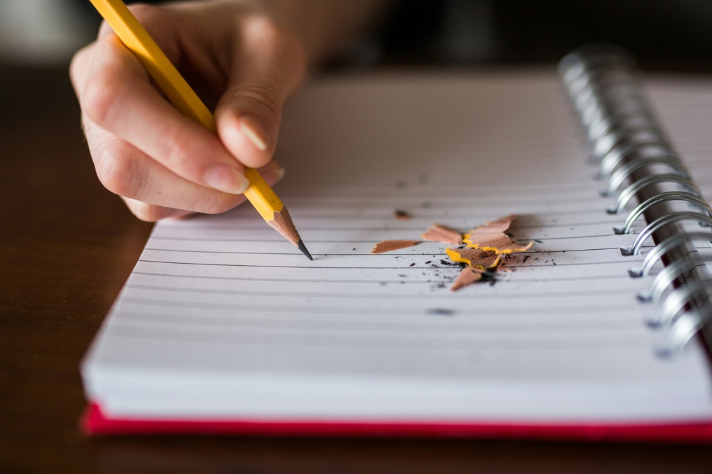 hand with pencil writing on notebook