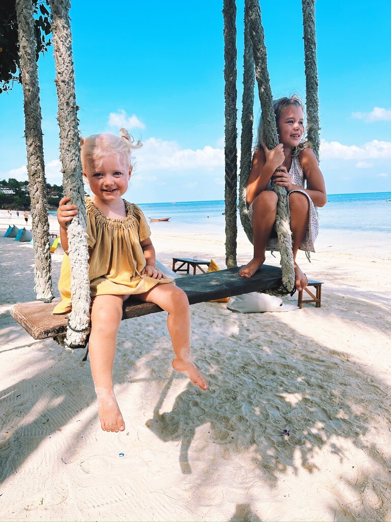 Two young girls sitting on a swing at a beach