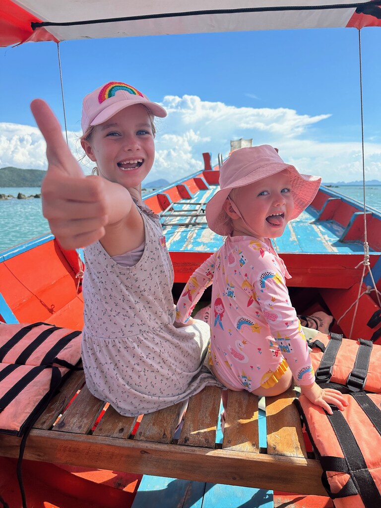 Two young girls with pink hats sitting in a long tail boat, visiting pig island with kids.