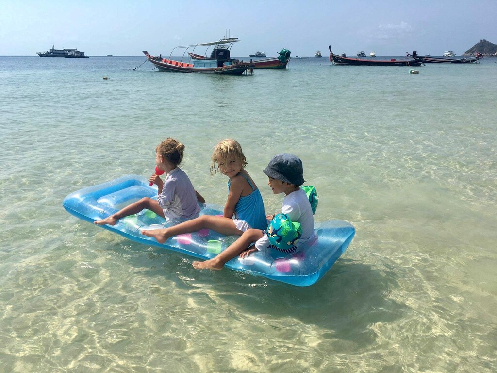 Three kids are enjoying a sunny day on the water, sitting on an inflatable raft.