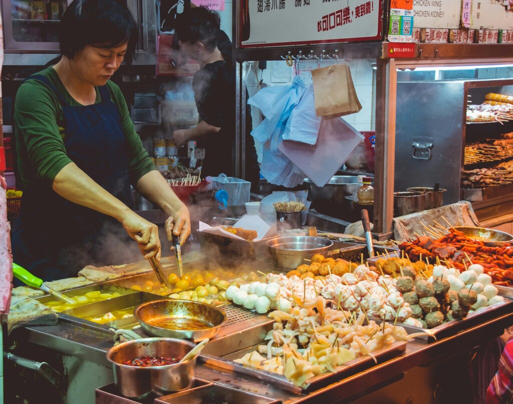 busy street food stall where a vendor is preparing various skewered and fried foods, eating out with kids in thailand