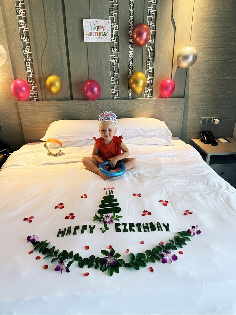 Little toddler girl sitting on a hotel bed that's decorated for her birthday