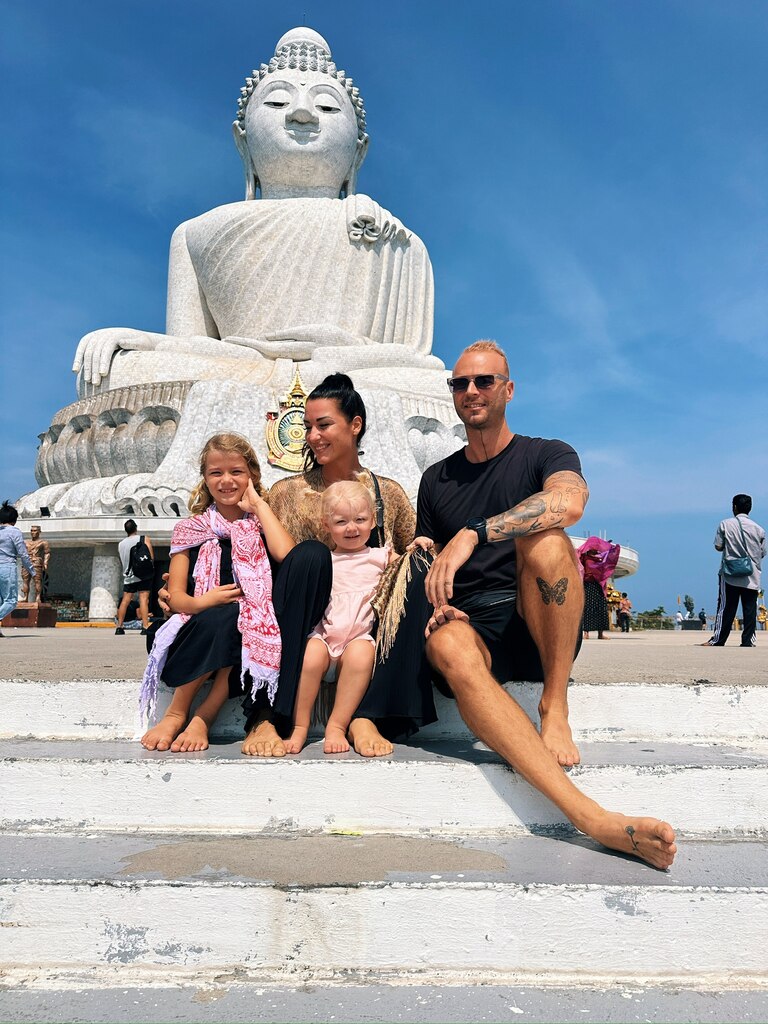 Family of four sitting in front of a white big buddha statue