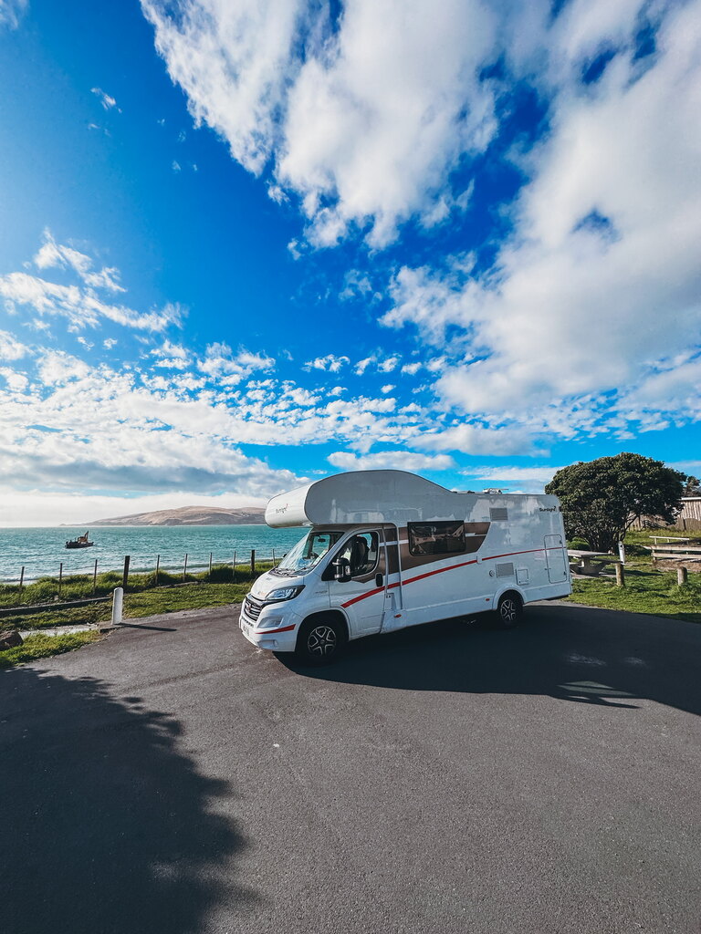 RV standing on a parking lot in front of the sea