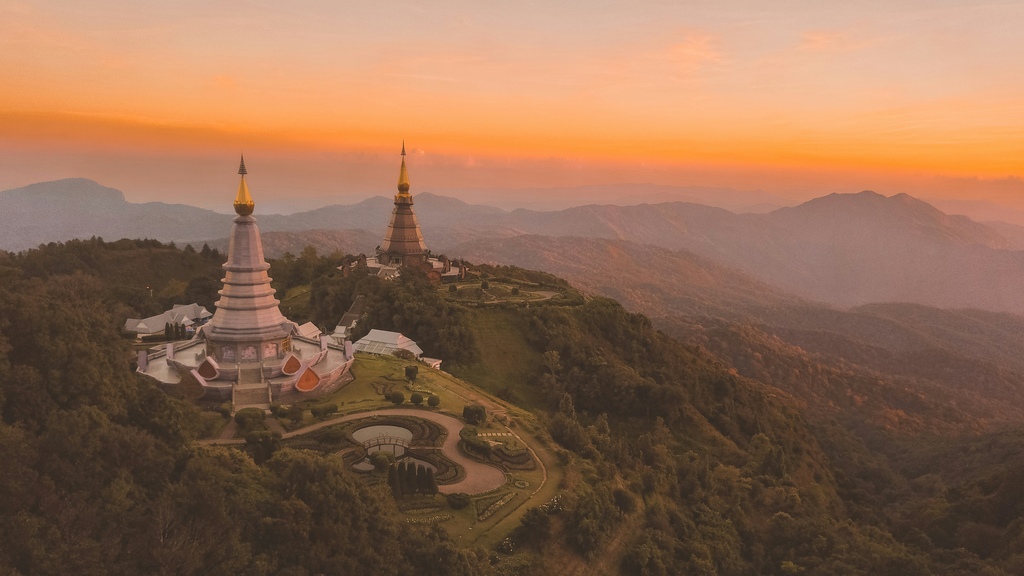 The image shows a breathtaking view of two large, intricately designed stupas on a lush green hillside at sunset