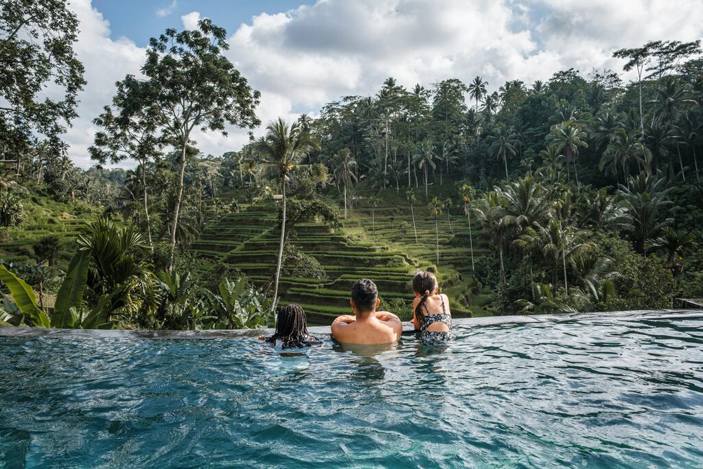 Fater with two girls in an infinity pool overlooking the jungle