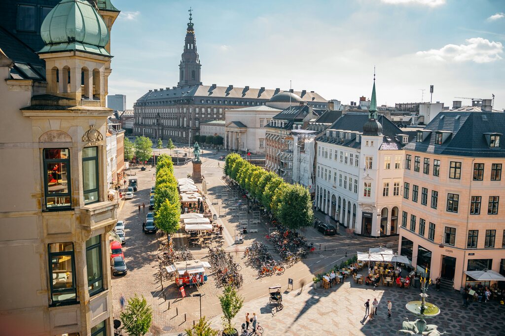 A scenic view of Christiansborg Palace in Copenhagen, with cobblestone streets, outdoor cafes, and bicycles parked along the sidewalk.