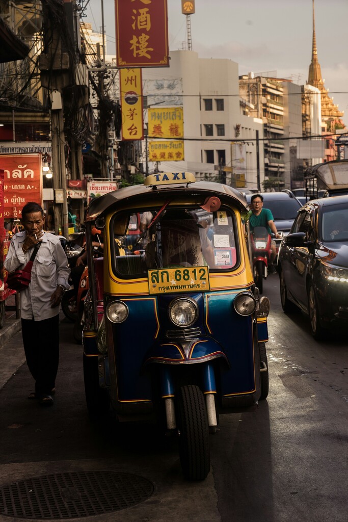 A traditional blue and yellow tuk-tuk taxi is parked on a busy street in Bangkok's Chinatown