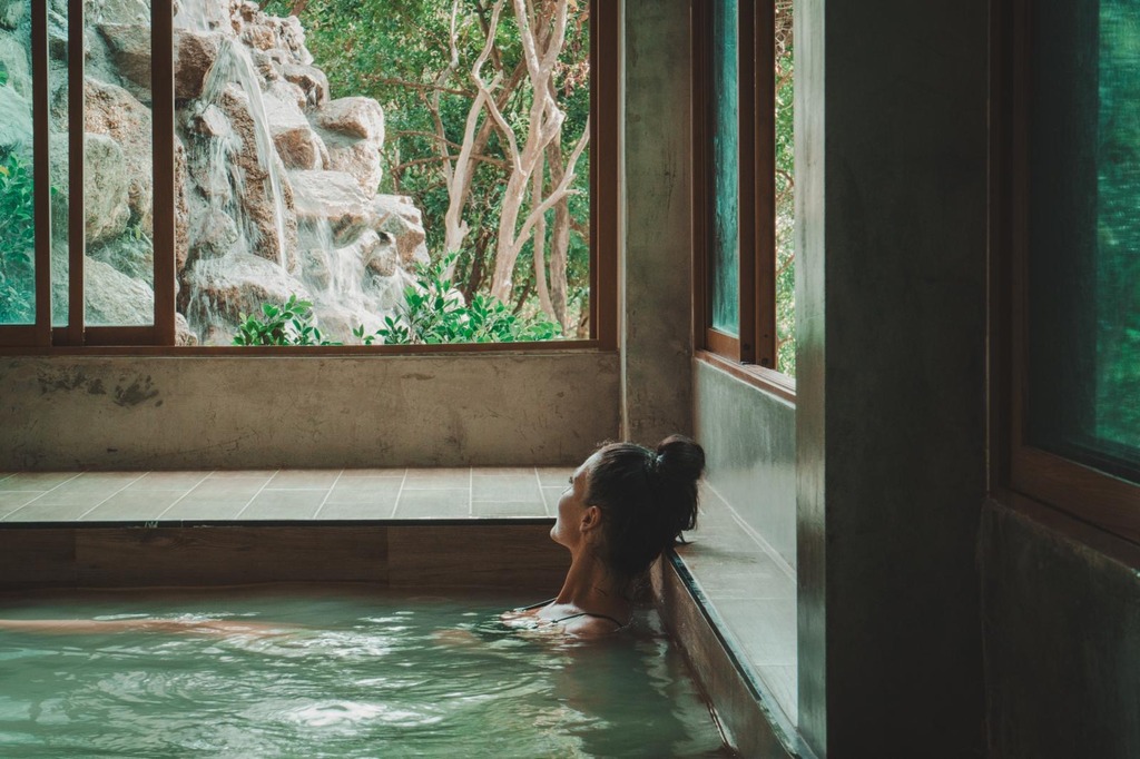 Woman bathing in an onsen pool, looking into the jungle.