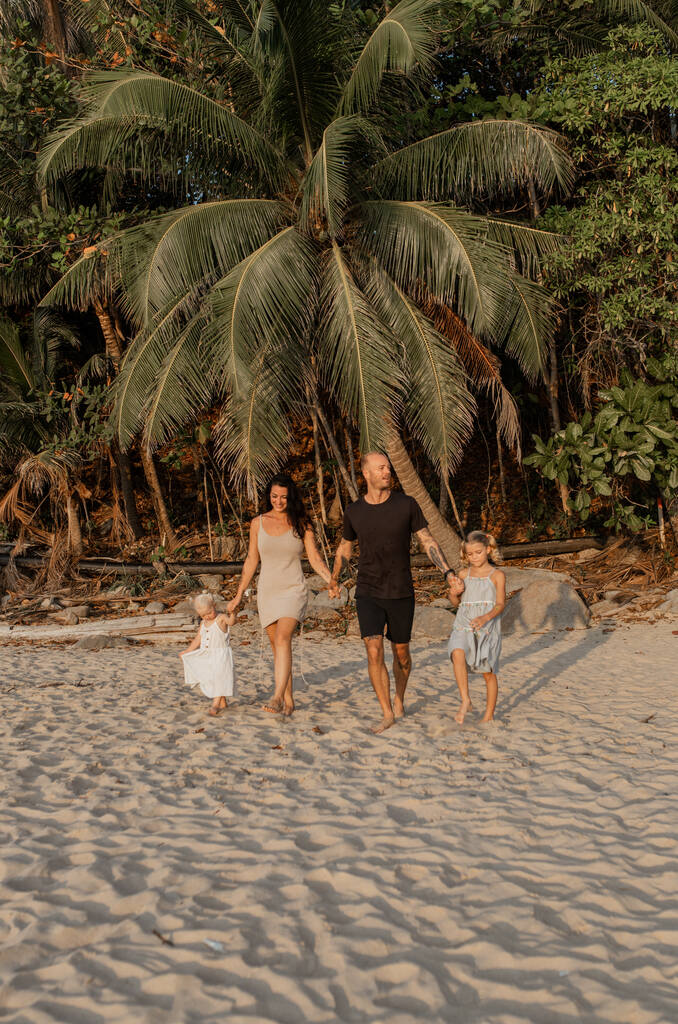 Family of four holding hands and walking at the beach.