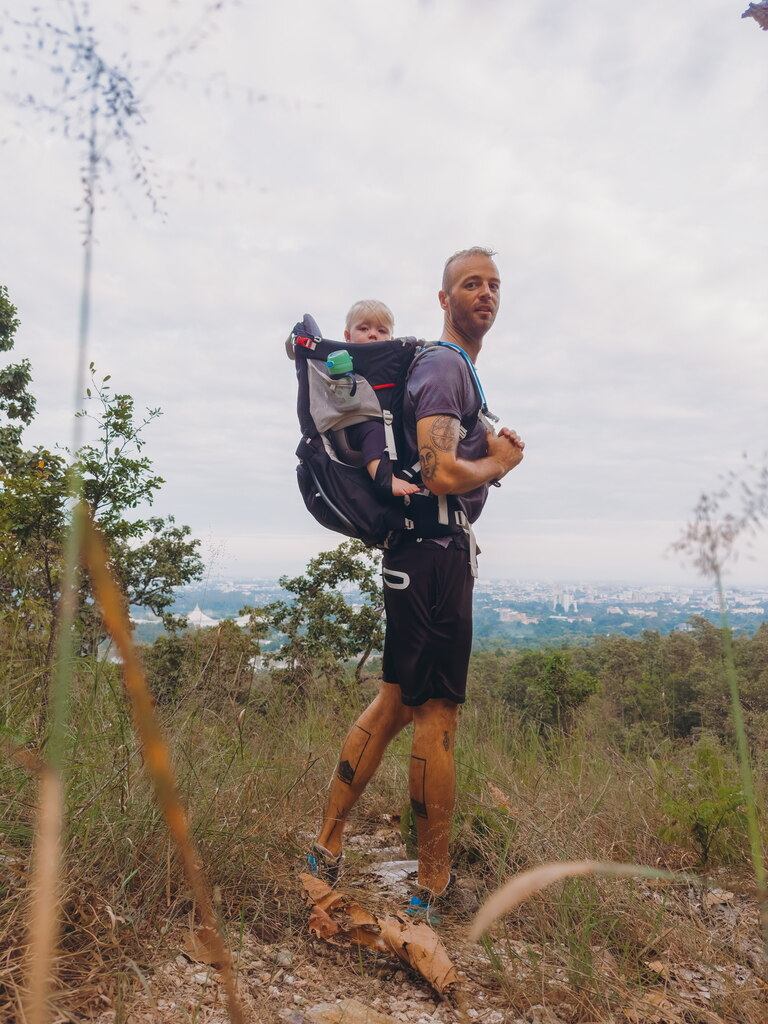 Dad with Baby in the back carrier, hiking on a green hill