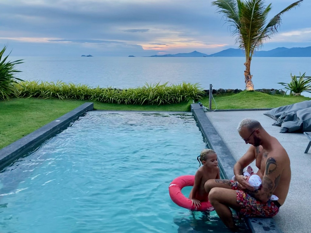 Dad in a pool with toddler and newborn daughters