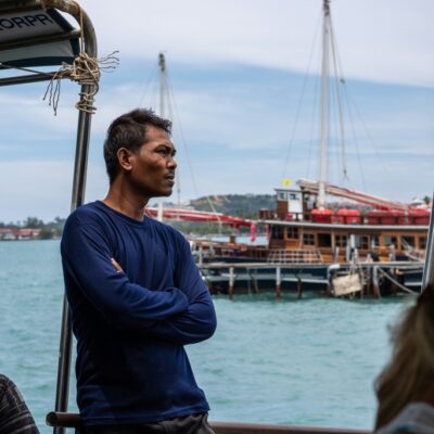 Thai man standing on the pier, a traditional thai boat in the background