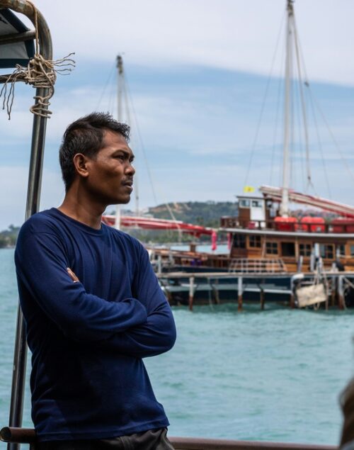 Thai man standing on the pier, a traditional thai boat in the background