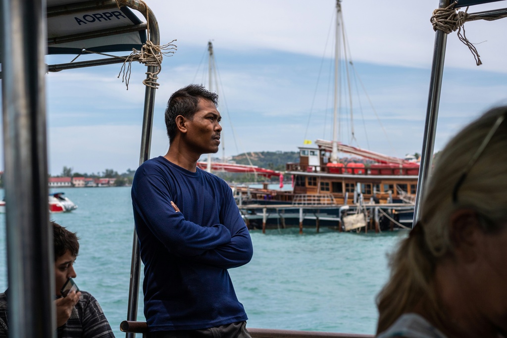 Thai man standing on the pier, a traditional thai boat in the background